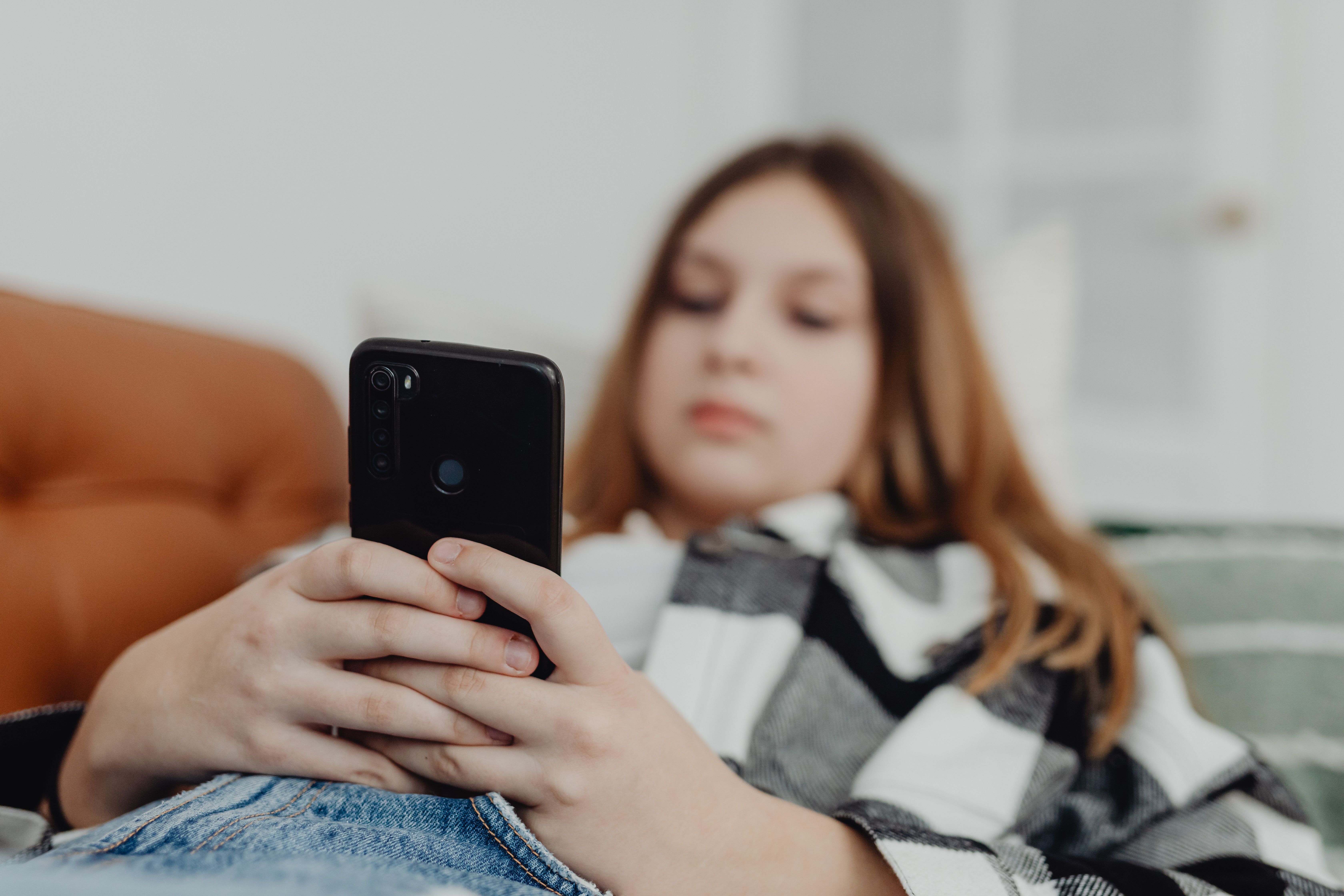 A teenage girl laying down and scrolling on her mobile phone